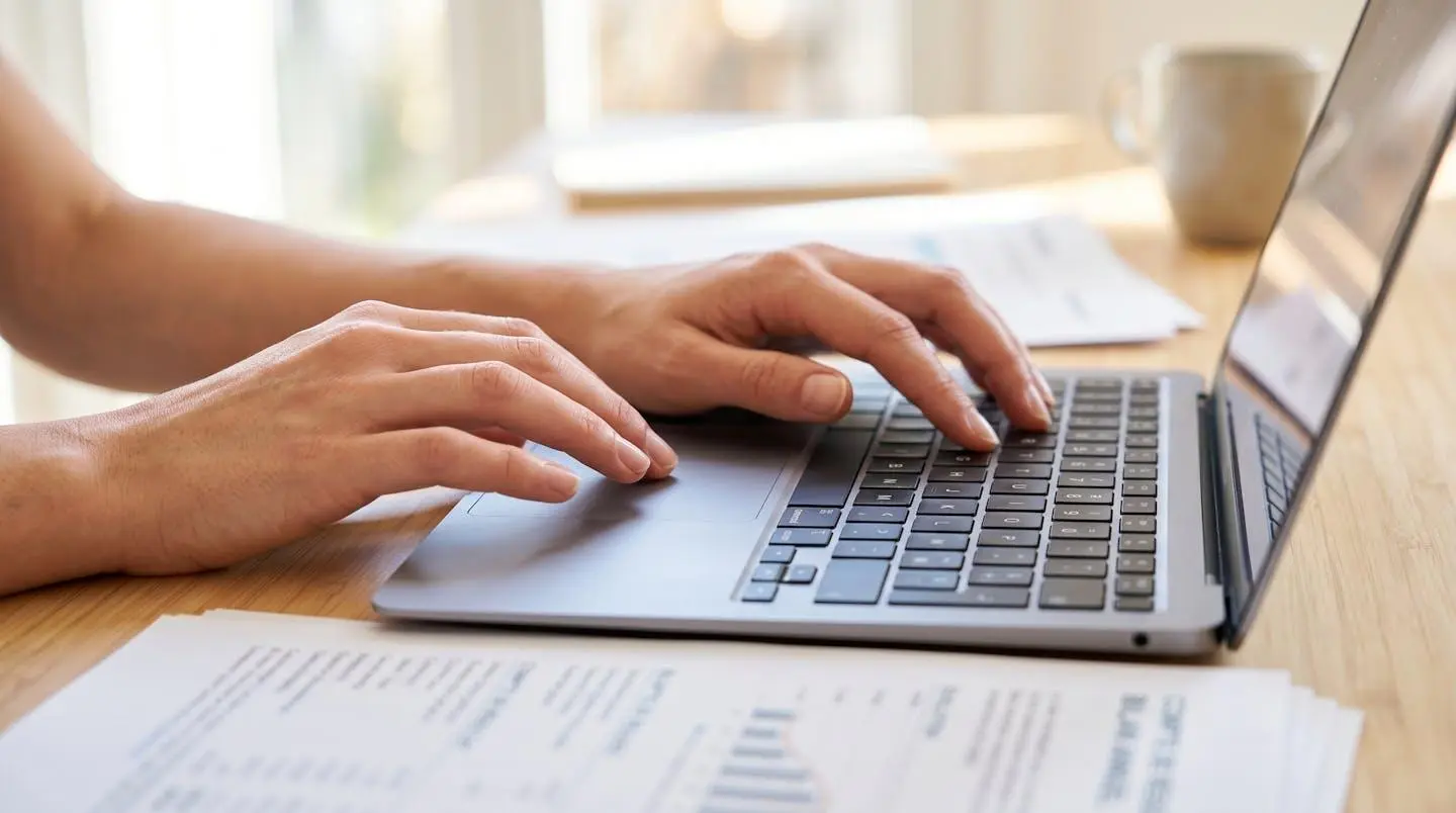 Gros plan sur des mains complétant un formulaire bancaire sur un bureau moderne avec ordinateur portable en arrière-plan flouté